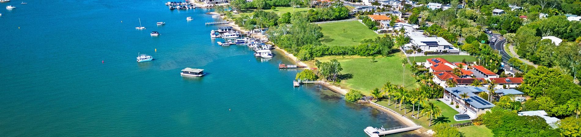 Aerial view of Cayman Quays holiday apartments at 100 Hilton Terrace and surrounding riverfront properties, highlighting our private guest jetty and boat mooring spaces on the Noosa River.