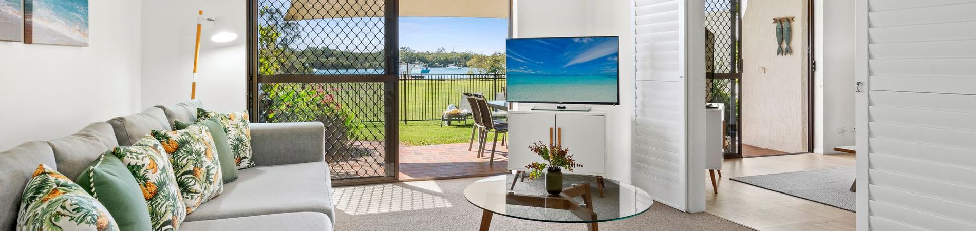 Townhouse Living Area, Paved Patio & Fenced Lawn Panoramic view of the four-bedroom holiday townhouse at Cayman Quays, showcasing the spacious living room transitioning out to a private paved patio, securely fenced grass lawn, and direct Noosa River views.