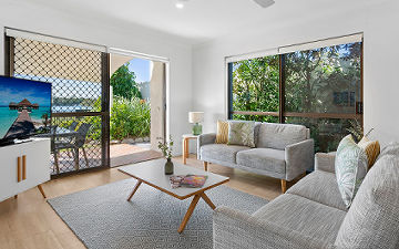 Spacious multi-level 4-bedroom holiday townhouse at Cayman Quays highlighting an expansive family lounge with sliding doors opening onto a large private patio courtyard with direct Noosa River views.