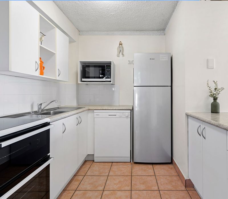 Fully self-contained holiday apartment kitchen equipped with a full-sized refrigerator, modern dishwasher, oven, microwave, crockery, glassware, and complete cutlery sets.