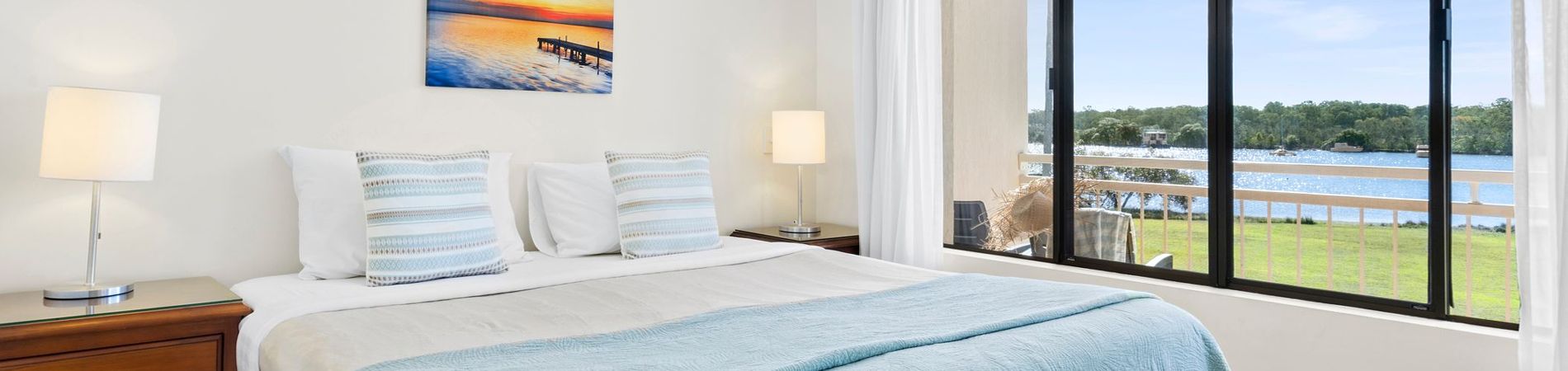 Special Accommodation Deals - Riverview Master Bedroom Bright master bedroom at Cayman Quays featuring a large window overlooking a private balcony with direct Noosa River views, featured on our holiday specials page.