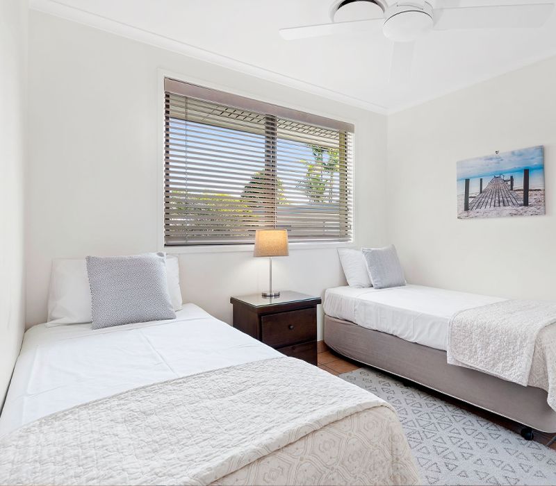 Bright second bedroom inside a Standard family apartment featuring twin single beds and windows with inward property views.