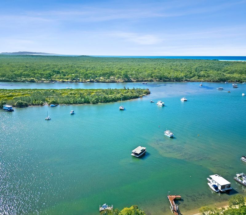 Expansive aerial panorama looking out from the private resort jetty across the full width of the Noosa River toward the Sunshine Coast hinterland mountain range.