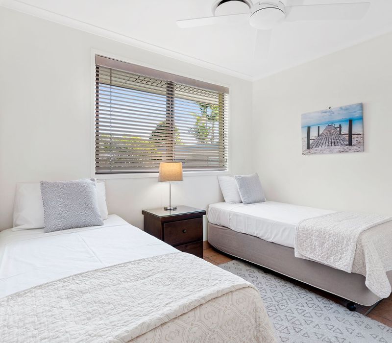 Comfortable second bedroom setup configured with two single beds and large windows showcasing refreshing outdoor views.