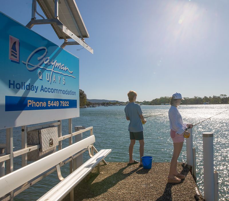 A young man and woman fishing from the private resort jetty on the edge of the absolute waterfront Noosa River.
