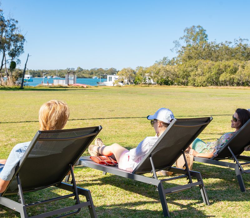 Guests relaxing on comfortable chaise lounges on the absolute waterfront grass lawn overlooking the majestic Noosa River.