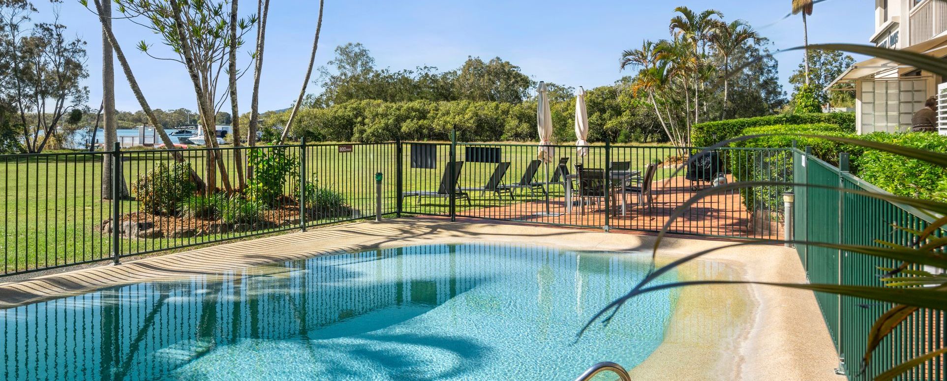 Panoramic landscape view of the Cayman Quays resort swimming pool and outdoor spa area with the Noosa River running in the distance.