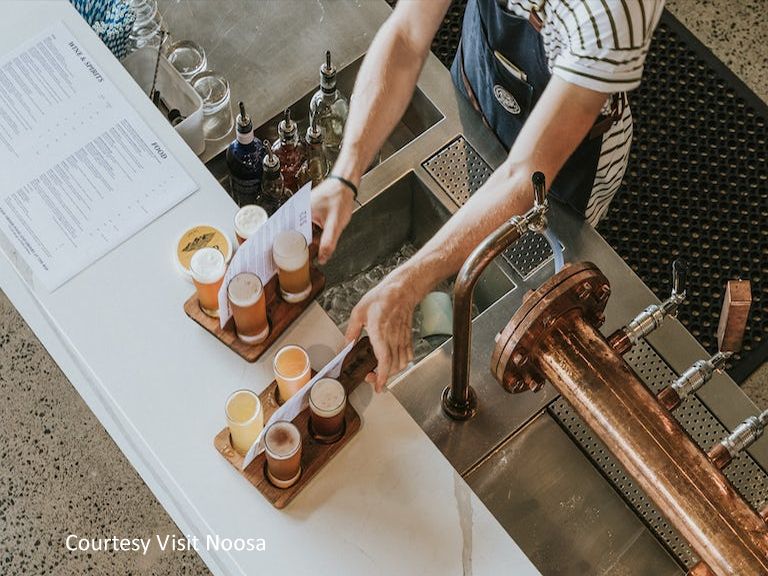 A bartender serving fresh craft beer tasting paddles and local dining platters at an indoor-outdoor waterfront bar in Noosaville.