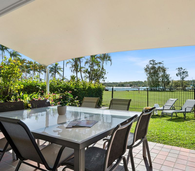 Outdoor al fresco dining table, chairs, and relaxation chaise lounges situated on the private townhouse patio overlooking the calm waters of the Noosa River.