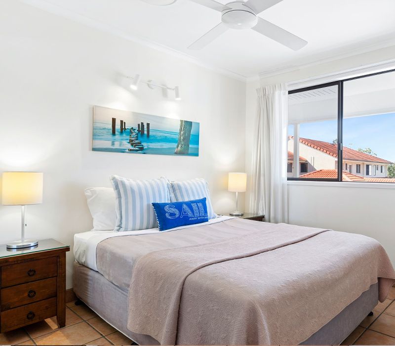 Bright and airy holiday apartment master bedroom featuring a queen size bed and large windows frame direct views of the Noosa River.
