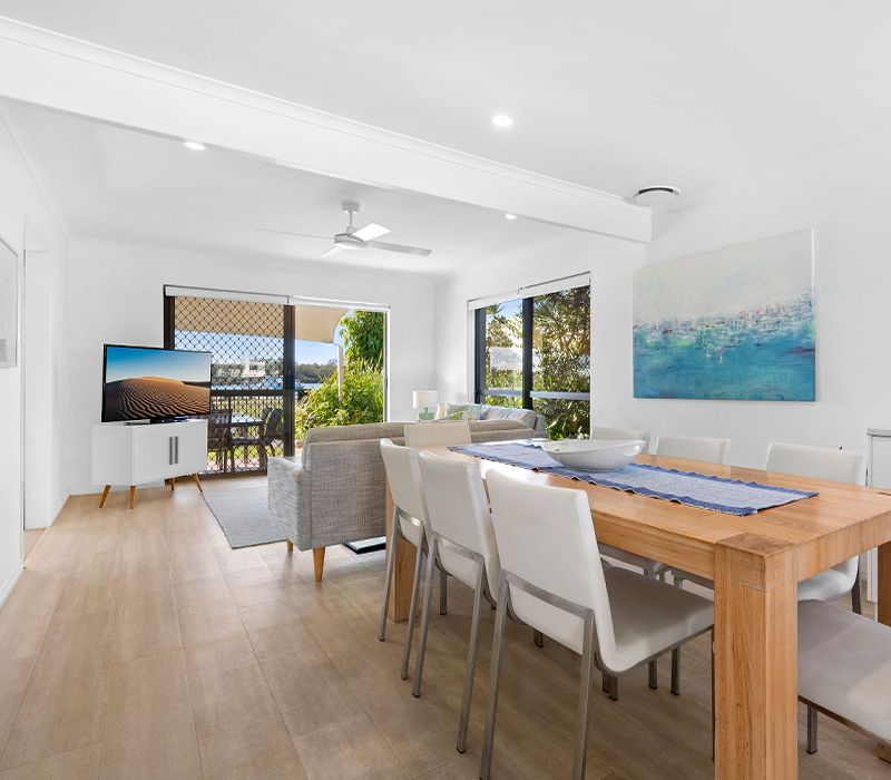 Light-filled open-plan interior of the Cayman Quays four-bedroom townhouse villa, seamlessly connecting the lounge, family dining layout, and scenic river view backdrop.