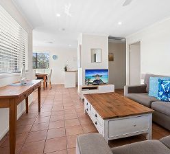 The large, light-filled open-plan interior of Unit One featuring a spacious family lounge, media entertainment space with TV, and dedicated holiday dining layout.